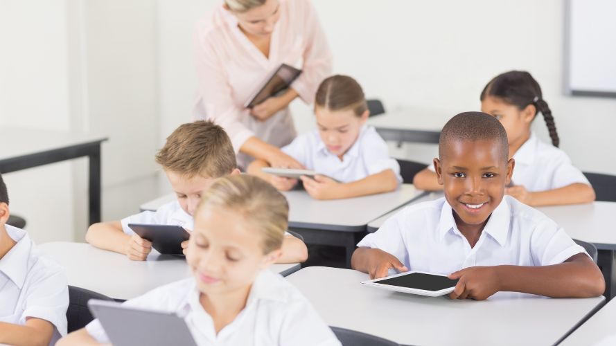 Class of children reading on tablets, one looks up and smiles
